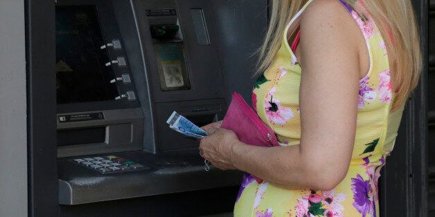 A woman uses an ATM of a bank after the government's decision last week to limit daily cash withdrawals to 60 euro ($66) in Athens, Tuesday, July 7, 2015. Greek Prime Minister Alexis Tsipras was heading Tuesday to Brussels for an emergency meeting of eurozone leaders, where he will try to use a resounding referendum victory to eke out concessions from European creditors over a bailout for the crisis-ridden country. (AP Photo/Petr David Josek)