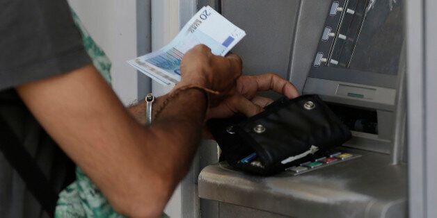 A man uses an ATM of a bank after the government's decision last week to limit daily cash withdrawals to 60 euro ($66) in Athens, Tuesday, July 7, 2015. Greek Prime Minister Alexis Tsipras was heading Tuesday to Brussels for an emergency meeting of eurozone leaders, where he will try to use a resounding referendum victory to eke out concessions from European creditors over a bailout for the crisis-ridden country. (AP Photo/Petr David Josek)