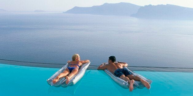 Holidaymakers on lilos in pool looking across bay, Oia, Santorini (Thira), Greek Islands, Greece, Europe