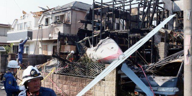 Firefighters (L) inspect a house damaged by fire caused after a light plane crashed into a residential area in Tokyo on July 26, 2015. The light single-engine plane crashed into a residential area in Tokyo, setting fire to several houses and reportedly killing three people. JAPAN OUT -- AFP PHOTO / JIJI PRESS (Photo credit should read JIJI PRESS/AFP/Getty Images)