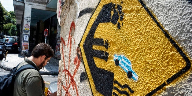 ATHENS, GREECE - JUNE 30: A man walks past anti-EU graffiti on June 30, 2015 in Athens, Greece. Greek voters will decide in a referendum next Sunday on whether their government should accept an economic reform package put forth by Greece's creditors. Greece has imposed capital controls with the banks being closed until the referendum and a daily limit of 60 euros has been placed on cash withdrawals from ATMs. (Photo by Milos Bicanski/Getty Images)