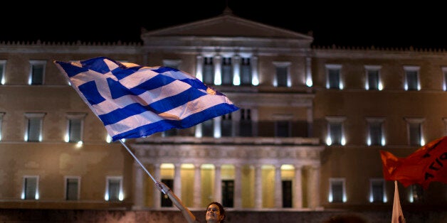 A supporter of the No vote waves a Greek flag in front of the parliament after the results of the referendum at Syntagma square in Athens, Sunday, July 5, 2015. Greeks overwhelmingly rejected creditors' demands for more austerity in return for rescue loans in a critical referendum Sunday, backing Prime Minister Alexis Tsipras, who insisted the vote would give him a stronger hand to reach a better deal. (AP Photo/Emilio Morenatti)