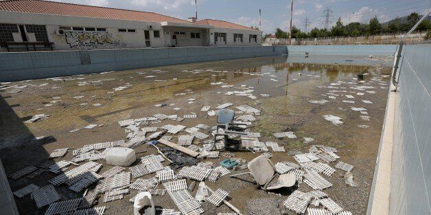 In this Tuesday, Aug. 5, 2014 photo, murky water and rubbish fill an abandoned training pool for athletes at the Olympic village in northern Athens. The latest government estimate sets the final cost of the Games at 8.5 billion euros, double the original budget but a drop in the ocean of the countryâs subsequent 320 billion-euro debt, which spun out of control after 2008. (AP Photo/Thanassis Stavrakis)