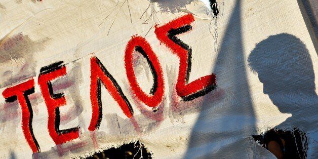 Anti-establishment protesters stand in front of a banner that reads, 'The End' during a demonstration against European Union's austerity in front of the Greek parliament in central Athens, on July 12, 2015. Divided eurozone leaders clashed over the fate of Greece on July 12 with a catastrophic exit from the single currency looming large as they struggled to reach a bailout deal with debt-hit Athens. AFP PHOTO / ANDREAS SOLARO (Photo credit should read ANDREAS SOLARO/AFP/Getty Images)