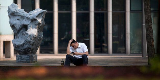 A man rubs his head while browsing his smartphone outside a brokerage house in Beijing Tuesday, July 7, 2015. Chinese stocks fell Tuesday despite official efforts to shore up slumping prices while other Asian markets were mixed after Greece's spiraling crisis weighed on Wall Street. (AP Photo/Andy Wong)