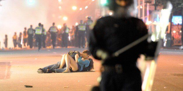 VANCOUVER, BC - JUNE 15: Riot police walk in the street as a couple kiss on June 15, 2011 in Vancouver, Canada. Vancouver broke out in riots after their hockey team the Vancouver Canucks lost in Game Seven of the Stanley Cup Finals. (Photo by Rich Lam/Getty Images)