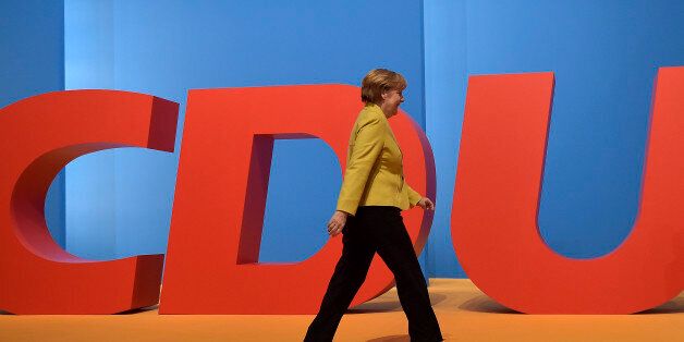 Chancellor and chairwoman of the German Christian Democrats, CDU, Angela Merkel, walks in front of a party logo during the 27th party convention in Cologne, Germany, Wednesday, Dec. 10, 2014. (AP Photo/Martin Meissner)