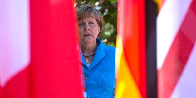 German Chancellor Angela Merkel waits near flags in the shade for G-7 leaders during arrivals for the G-7 summit at Schloss Elmau hotel near Garmisch-Partenkirchen, southern Germany, Sunday, June 7, 2015. The two-day summit will address such issues as climate change, poverty and the situation in Ukraine. (AP Photo/Virginia Mayo)