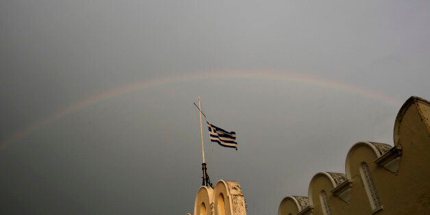 A Greek flag flies on top of the municipality market with rainbow on the background on Kos island, Greece, Friday, May 29, 2015. Bank deposits in Greece have hit their lowest in more than a decade, according to data released Friday, as Greeks concerned about the painfully slow pace of their government's talks with bailout creditors withdrew savings in an orderly but steady flow.(AP Photo/Petros Giannakouris)