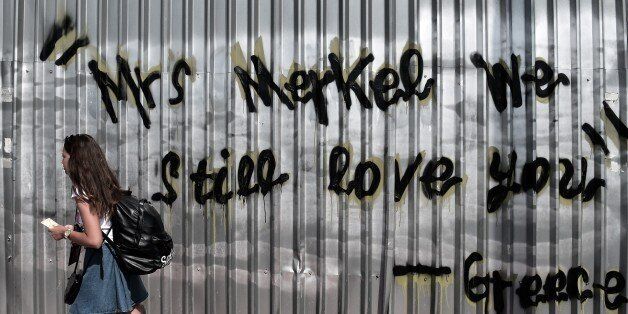 A young woman walks past a graffiti reading 'Mrs Merkel we still love you - Greece' in central Athens on June 19, 2015. The European Central Bank's decision-making governing council will hold an emergency session on June 19 to discuss a request from the Bank of Greece for an increase in liquidity to Greek banks. AFP PHOTO / ARIS MESSINIS (Photo credit should read ARIS MESSINIS/AFP/Getty Images)