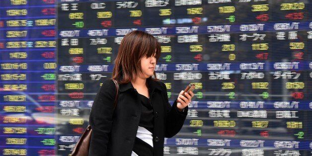 A woman uses her smart phone before a share prices board in Tokyo on April 9, 2015. Japan's share prices rose 147.91 points to close at 19,937.72 points at the Tokyo Stock Exchange, thanks to a weaker yen, with the benchmark Nikkei index approaching the psychologically important 20,000 level last seen in 2000. AFP PHOTO / Yoshikazu TSUNO (Photo credit should read YOSHIKAZU TSUNO/AFP/Getty Images)
