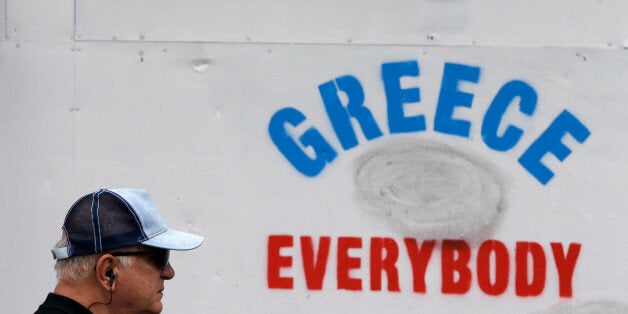 An elderly man passes a graffiti outside an old bank in Athens, Tuesday, June 30, 2015. Greek Finance Minister Yanis Varoufakis confirmed that the country will not make its payment due later to the International Monetary Fund. With banks shut and Greeks limited to cash withdrawals of 60 euros ($67) per day, long lines formed once more at ATM machines. (AP Photo/Thanassis Stavrakis)