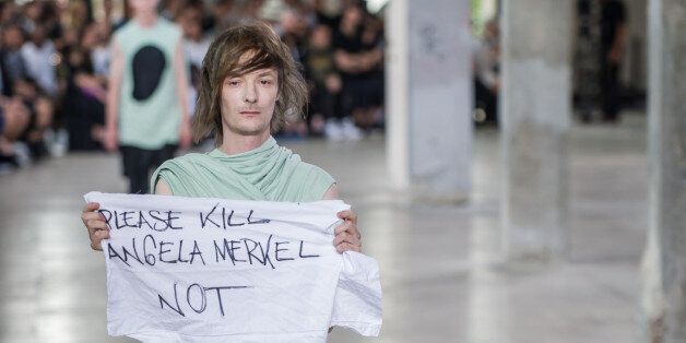 A model wears a creation by Rick Owens and holds a banner reading