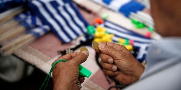 A man holds coins as he prepares to buy Greek flags during a rally organized by supporters of the YES vote to the upcoming referendum in Athens, Tuesday, June 30, 2015. Greece is set to become the first developed nation to not pay its debts to the International Monetary Fund on time, as the country sinks deeper into a financial emergency that has forced it put a nationwide lockdown on money withdrawals. (AP Photo/Daniel Ochoa de Olza)