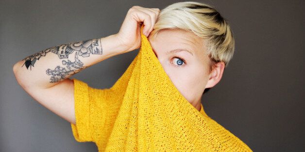 Young tattooed woman pulling jumper over her face.