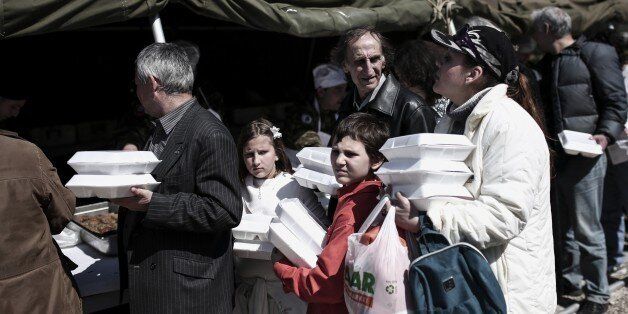 People line up to take free food which is distributed at a military camp near Athens on April 12, 2015. Greece's Defense ministry organized a free meal for the poor on Orthodox Easter. AFP PHOTO / ANGELOS TZORTZINIS (Photo credit should read ANGELOS TZORTZINIS/AFP/Getty Images)