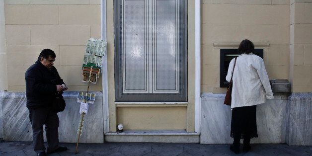 A customer uses an ATM machine outside a bank as a street lottery vendor stands in central Athens, on Wednesday, Feb. 25, 2015. Greece cleared a major hurdle on Tuesday after the finance ministers of the other 18 eurozone countries approved a list of policy goals Greek Finance Minister Yanis Varoufakis sent to Brussels and granted the four-month bail out extension. The list is being used as a starting point for the creation of new measures Greek parliament will have to vote into law.(AP Photo/Petros Giannakouris)