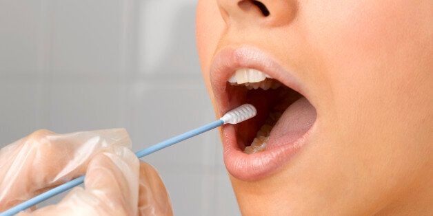 Person holding DNA swab in young woman's mouth, close up of mouth, studio shot