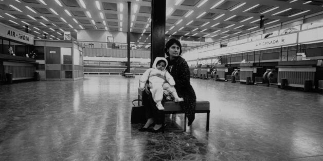 February 1968: An Asian woman and her young baby, immigrants to Britain, sit in a deserted London airport. (Photo by Roy Jones/Evening Standard/Getty Images)