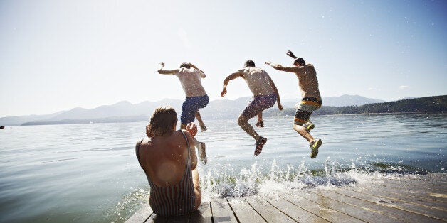 Woman sitting on the edge of floating dock while three men jump into water