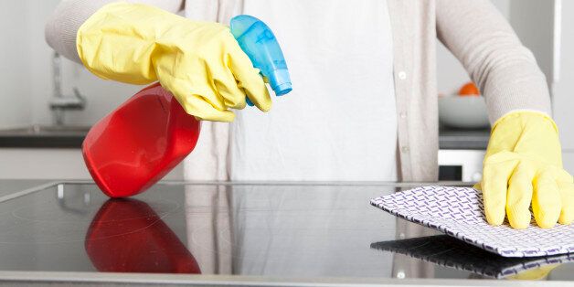 Woman wearing gloves cleaning ceramic glass cooktop with spray