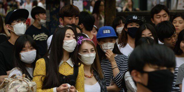 People wearing face masks watch a K-Pop performance on a street in the popular student area of Hongdae in Seoul on June 7, 2015. South Korea reported its fifth death from MERS as the government on June 7 vowed 'all-out' measures to curb the outbreak that was threatening to spread nationwide, including tracking mobile phones of those in quarantine. AFP PHOTO / Ed Jones (Photo credit should read ED JONES/AFP/Getty Images)