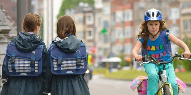 Two girls in school uniform encounter a colorfully dressed girl on a bike.