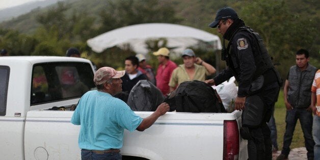 A member of the Guerrero state police (R) inspects the back of a truck at a checkpoint entering the city of Chilapa, in the Mexican state of Guerrero, on the eve of midterm elections, on June 6, 2015. Meanwhile, a self-defense militia was attacked by a rival faction in southern Mexico on June 6 leaving at least 10 people dead, witnesses said, amid tensions in the region on the eve of elections. While the bloodshed in the village of Xolapa did not appear linked to the June 7 congressional, gubernatorial and municipal elections, it occurred in a state plagued by violence and protests ahead of the vote. AFP PHOTO / PEDRO PARDO (Photo credit should read Pedro PARDO/AFP/Getty Images)