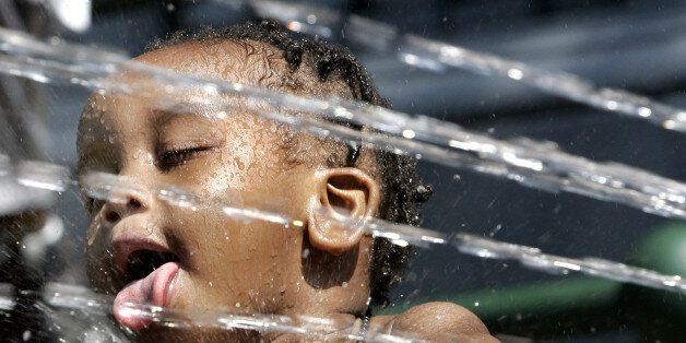 Two-year-old Jaivel Pope gets splashed as he trys to get a drink out of the spray from an open fire hydrant as young kids in Harlem try to beat the heat 01 August 2006 in New York. New York, Boston, Washington, DC, and much of the US East Coast will face record- breaking temperatures that may top 100 degrees(37.7c). The extreme temperatures are also taxing the already strained power system as electrical demand runs high to keep air conditioning running. (Photo credit should read TIMOTHY A. CLARY/AFP/GettyImages)