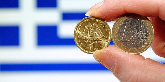 A photo taken on february 15, 2012 shows a person holding a 1 euro coin (R) and Greek 1 drachma coin in front of a Greek national flag. AFP PHOTO PHILIPPE HUGUEN (Photo credit should read PHILIPPE HUGUEN/AFP/Getty Images)