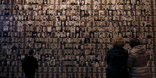 In this photo taken Saturday, March 21, 2015, visitors look at portraits of victims at the Holocaust Museum in the town of Kalavryta, western Greece. It was 1943 and the Nazis were deporting Greece's Jews to death camps in Poland. Hitler's genocidal accountants reserved a chilling twist: The Jews had to pay their train fare. The bill for 58,585 Jews sent to Auschwitz and other camps exceeded 2 million Reichsmark â more than 25 million euros ($27 million) in today's money. For decades, this