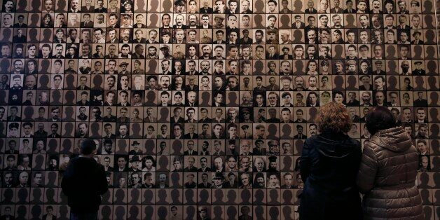 In this photo taken Saturday, March 21, 2015, visitors look at portraits of victims at the Holocaust Museum in the town of Kalavryta, western Greece. It was 1943 and the Nazis were deporting Greece's Jews to death camps in Poland. Hitler's genocidal accountants reserved a chilling twist: The Jews had to pay their train fare. The bill for 58,585 Jews sent to Auschwitz and other camps exceeded 2 million Reichsmark â more than 25 million euros ($27 million) in today's money. For decades, this