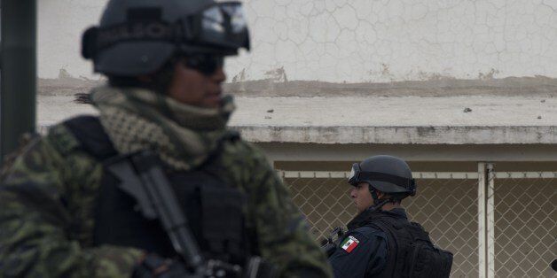 A federal policeman (R) and a soldier (L) stand guard before the presentation of Juan Manuel Rodriguez Garcia (out of frame), aka 'Juan Perros', an alleged leader of the Gulf drug cartel, during his presentation for the press at the hangar of the Attorney General's office in Benito Juarez International Airport in Mexico City on May 25, 2014. According to the statement read during his presentation, Rodriguez Garcia was arrested in Tamaulipas. AFP PHOTO/ Yuri CORTEZ (Photo credit should rea