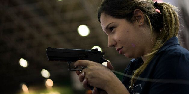 A woman jokingly holds a pistol as she is photographed by a friend at the LAAD Defence and Security International Exhibition in Rio de Janeiro, Brazil, Tuesday, April 14, 2015. (AP Photo/Felipe Dana)