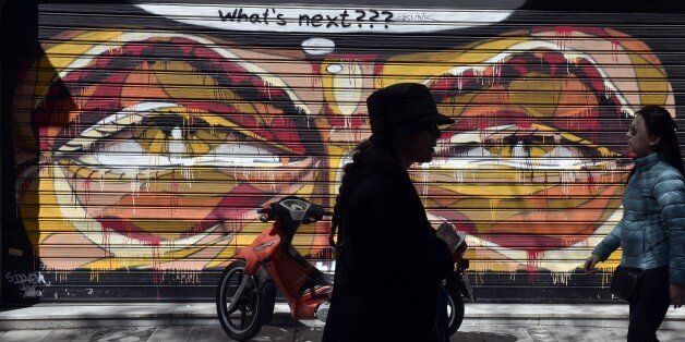 Women walk past shut down store with graffiti on it in central Athens on March 30, 2015. Cash-strapped Greece wrangles with its eurozone partners over a new package of economic reforms needed to unlock a vital 7.2-billion-euro tranche of bailout funds ahead of a crucial week of negotiations.AFP PHOTO / LOUISA GOULIAMAKI (Photo credit should read LOUISA GOULIAMAKI/AFP/Getty Images)
