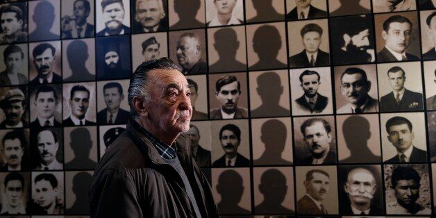 In this photo taken Saturday, March 21, 2015, Georgios Dimopoulos, 85, a survivor of the Kalavryta massacre poses for a photograph next to the portraits of his father (fourth row, fifth column) and his uncle (fifth row, third column) at the Holocaust Museum in the town of Kalavryta ,western Greece. On December 13, 1943, more than 500 males aged 14 and over were machine-gunned in the greatest massacre perpetrated by the occupying German troops. Greek Prime Minister Alexis Tsipras, who will meet C