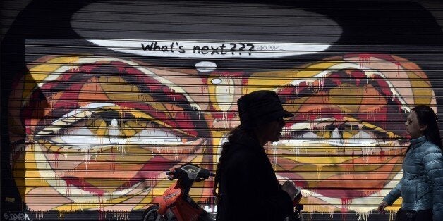 Women walk past shut down store with graffiti on it in central Athens on March 30, 2015. Cash-strapped Greece wrangles with its eurozone partners over a new package of economic reforms needed to unlock a vital 7.2-billion-euro tranche of bailout funds ahead of a crucial week of negotiations.AFP PHOTO / LOUISA GOULIAMAKI (Photo credit should read LOUISA GOULIAMAKI/AFP/Getty Images)