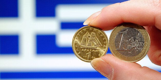 A photo taken on february 15, 2012 shows a person holding a 1 euro coin (R) and Greek 1 drachma coin in front of a Greek national flag. AFP PHOTO PHILIPPE HUGUEN (Photo credit should read PHILIPPE HUGUEN/AFP/Getty Images)