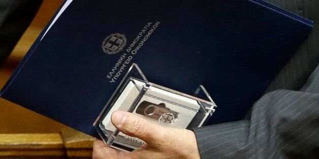 Greece's Finance Minister Gikas Hardouvelis, holds a clear case with two flash drives containing the new state budget for 2015 at the Greek parliament in Athens, on Friday, Nov. 21, 2014. Greeceâs government has submitted its 2015 budget to Parliament, predicting the debt-ridden countryâs economy will emerge from recession with growth of 2.9 percent and a primary surplus _ income without taking into account interest payments on outstanding debt _ of 3 percent of gross domestic product. The blue envelop reads ''Hellenic Republic, Finance Ministry.'' (AP Photo/Thanassis Stavrakis)