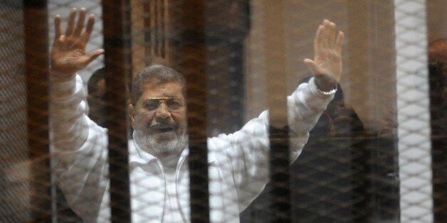 Egypt's deposed Islamist president Mohamed Morsi waves from inside the defendants cage during his trial at the police academy in Cairo on January 8, 2015. An Egyptian court is to deliver a verdict on April 21 in the trial of Morsi and 14 others charged with inciting the killing of protesters, judicial officials said. AFP PHOTO / STR (Photo credit should read STR/AFP/Getty Images)