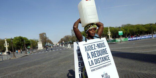 Gambian woman Siabatou Sanneh displays a sandwich board which translates as 'Help us to reduce the distance' as she carries a jerrycan of water on her head while walking the route of the 39th Paris Marathon in Paris, on April 12, 2015, to raise awareness for the cause of charity 'Water for Africa'. Siabatou Sanneh's symbolic participation in the 39th Paris Marathon while carrying a jerrycan of water on her head was to raise awarness of the plight of many people living in Africa who must walk