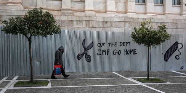 A pedestrians passes graffiti reading 'Cut The Debt, IMF Go Home' on corrugated fencing outside the Academy of Athens in Athens, Greece, on Saturday, Feb. 14, 2015. Greece's euro-area creditors voiced skepticism that a breakthrough was within reach over financing Europe's most indebted state. Photographer: Yorgos Karahalis/Bloomberg via Getty Images