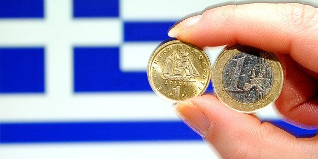 A photo taken on february 15, 2012 shows a person holding a 1 euro coin (R) and Greek 1 drachma coin in front of a Greek national flag. AFP PHOTO/PHILIPPE HUGUEN (Photo credit should read PHILIPPE HUGUEN/AFP/Getty Images)