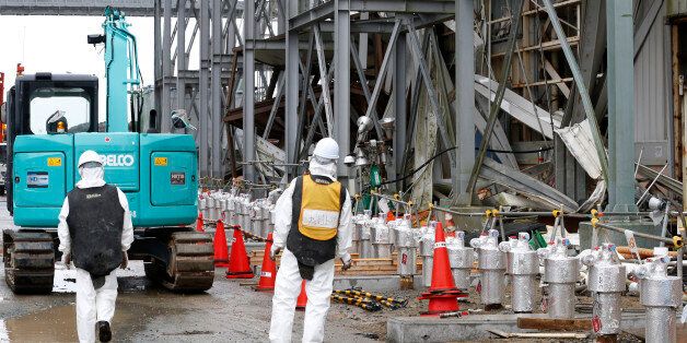 Workers wearing protective gears stand outside the Unit 4 reactor at the Fukushima Dai-ichi nuclear power plant in Okuma, Fukushima prefecture, northeastern Japan, Wednesday, Nov. 12, 2014. More than three years into Japan's massive cleanup of the tsunami-damaged nuclear plant, only a tiny fraction of the workers are focused on the key tasks of dismantling the broken reactors and removing radioactive fuel rods. (AP Photo/Shizuo Kambayashi, Pool)