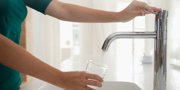 Woman filling glass of water at kitchen sink, cropped