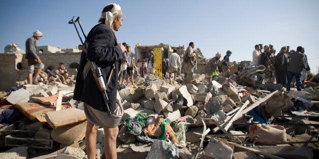 A Houthi Shiite fighter stand guard as people search for survivors under the rubble of houses destroyed by Saudi airstrikes near Sanaa Airport, Yemen, Thursday, March 26, 2015. Saudi Arabia launched airstrikes Thursday targeting military installations in Yemen held by Shiite rebels who were taking over a key port city in the country's south and had driven the embattled president to flee by sea, security officials said. (AP Photo/Hani Mohammed)