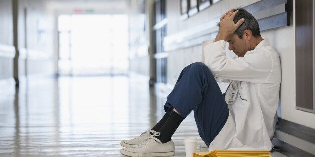 Doctor sitting on floor in hospital corridor with head in hands