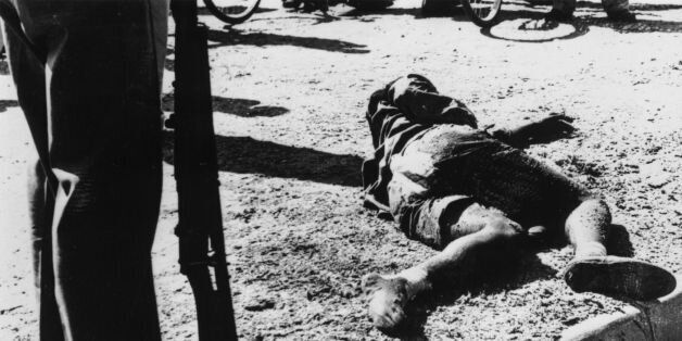 An armed man stands beside the body of one of the sixty-nine black South Africans killed by police in the massacre at Sharpeville, South Africa, March 21, 1960. The massacre was provoked by peaceful demonstrations against laws requiring blacks to carry passes at all times. (Photo by Central Press/Getty Images)