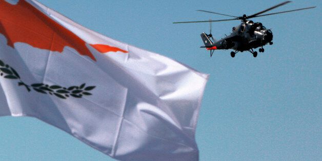 A military helicopter hovers over the parade route as the national flag of Cyprus' flies during the annual Cyprus Independence Day military parade in the divided capital of Nicosia, Cyprus, Tuesday, Oct. 1, 2013. Authorities in bailed-out Cyprus decided against tanks and other vehicles from participating in the annual parade to mark the countryâs 53rd year of independence from British colonial rule, in an effort to save money. (AP Photo/Petros Karadjias)