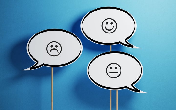 White chat bubble with wooden stick on blue background. There are various smiley faces on the speech bubbles. Horizontal composition with copy space.